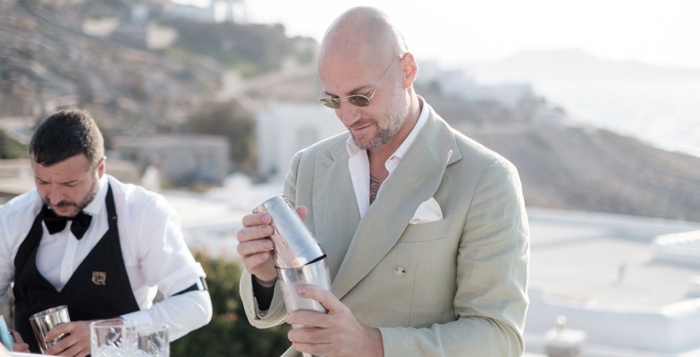 Giorgio Tosato, professional mixologist from Philoxenia Events London, preparing cocktails at a luxury bar for an American wedding in a private villa in Mykonos, Greece, with a stunning sea view