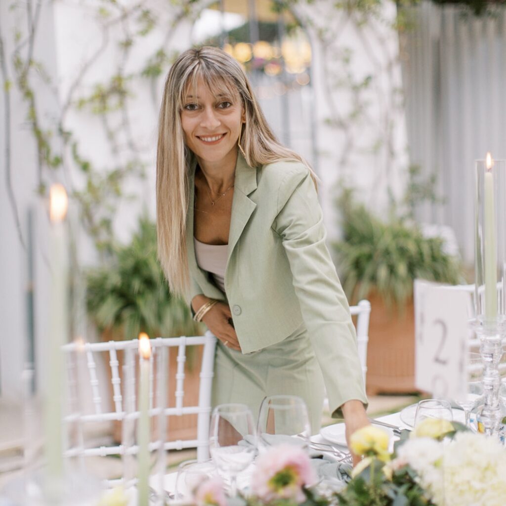 Silia, wedding planner from Philoxenia Events London, arranging an elegant Amalfi Coast wedding table with candles, flowers, and glassware