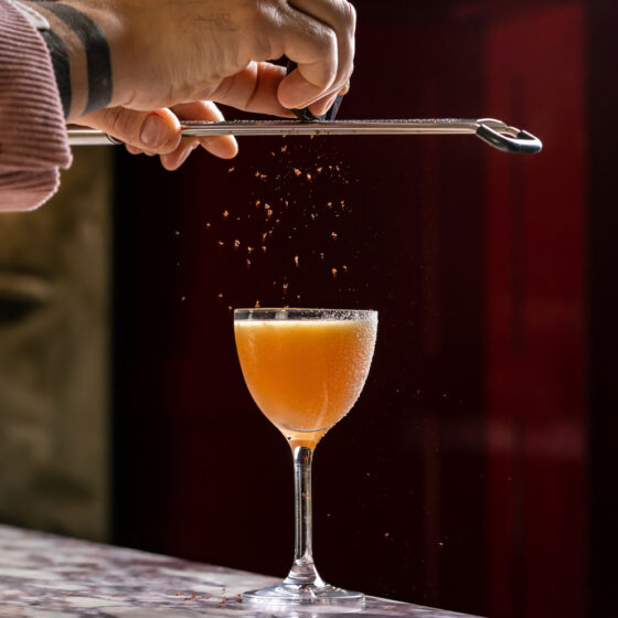 Senior mixologist from Philoxenia Events preparing a signature tequila cocktail garnished with grated cocoa using all homemade ingredients